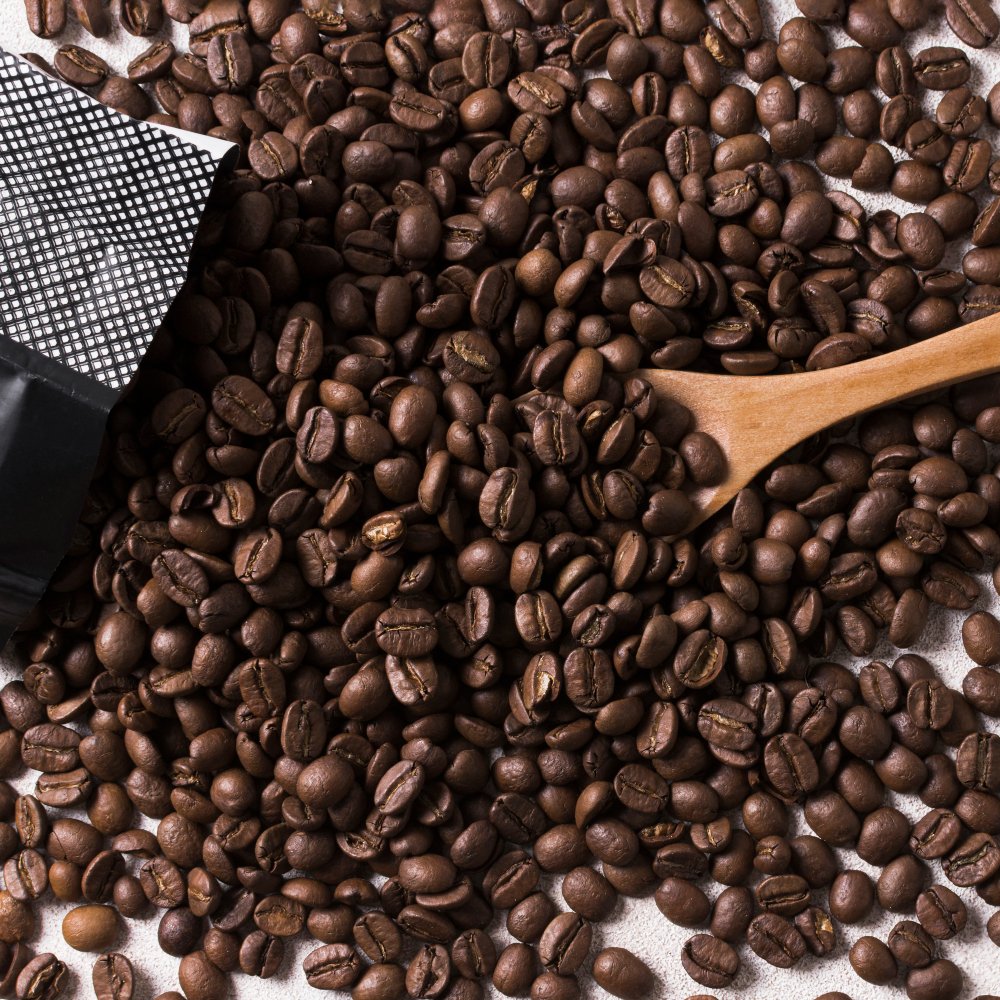 A wooden spoon rests beside medium roast whole coffee beans, showcasing their rich color and texture.