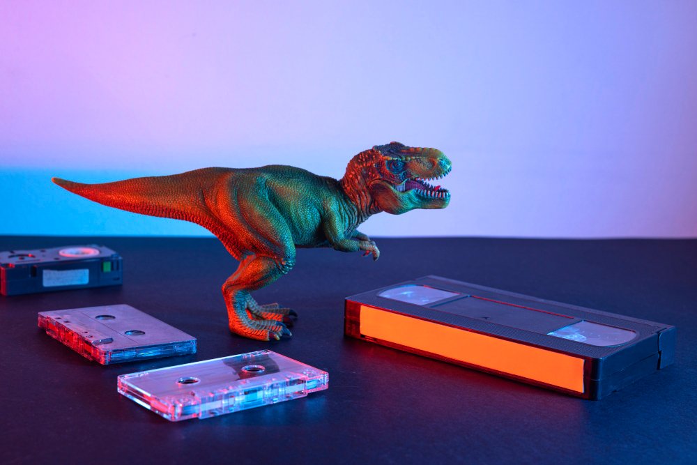 A toy dinosaur next to a cassette tape, showcasing the thrilling world of premium dinosaur excavators and RC rock crawlers.