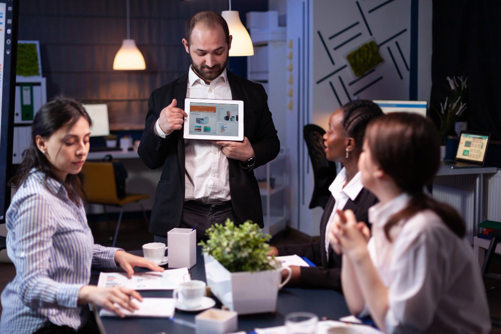 A man presents a tablet to his colleagues in a collaborative setting at a top digital marketing agency.