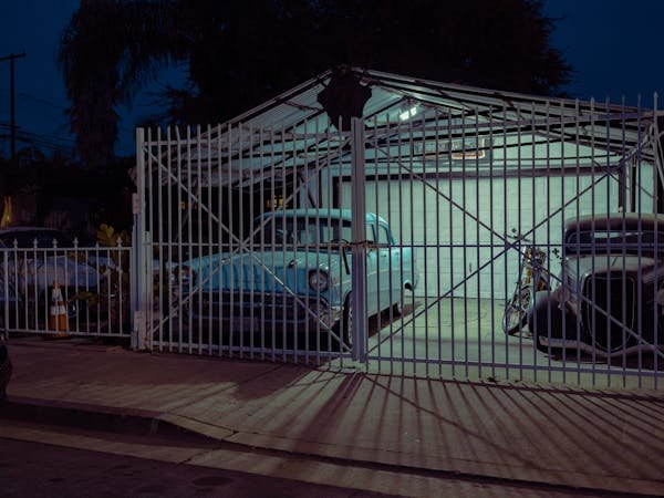 A driveway with a parked car is enclosed by a white fence and gate, representing Houston's top-rated garage door services.